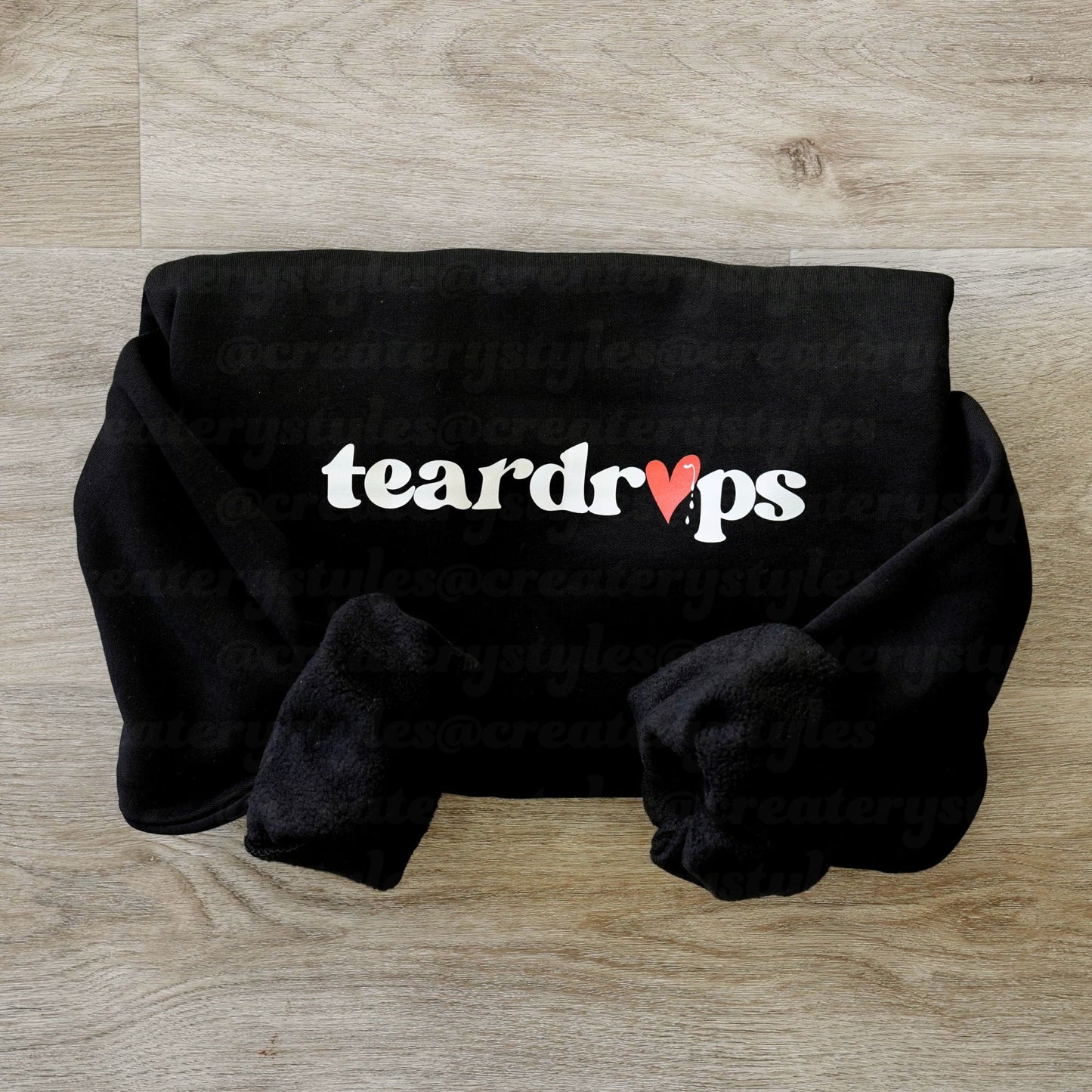 Black plush blanket with 'teardrops' text on a wooden surface